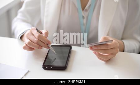 Cropped image of a female worker or businesswoman using stylus pen with smartphone, holding a credit card to connect her account with mobile applicati Stock Photo