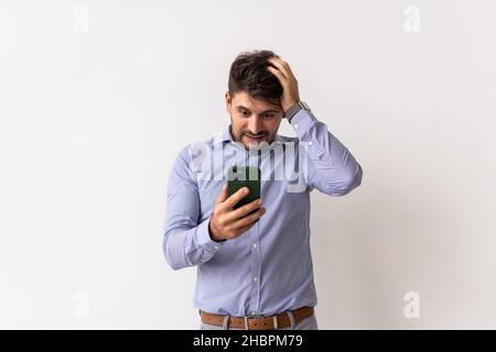 Close up portrait of handsome young man in white t-shirt, holding smartphone, looking scared and confused reading text message or e-mail Stock Photo