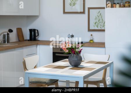 Image of beautiful flowers in vase on the kitchen table in empty domestic kitchen Stock Photo