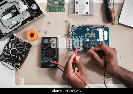 Layout of hands of repairman soldering tiny details on circuit board of electronic device by workplace Stock Photo