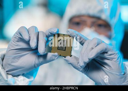 Gloved hands of contemporary scientist or it-engineer in protective workwear holding microchip Stock Photo