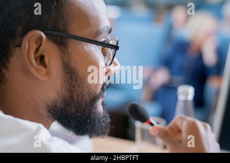Part of face of young bearded speaker in eyeglasses making speech in front of audience at conference or summit Stock Photo