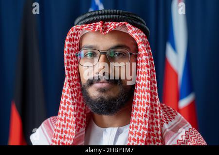 Contemporary young delegate or political leader in turban standing in front of camera while standing against flags Stock Photo