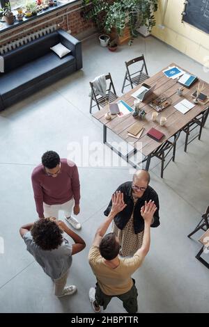Two young co-workers touching by hands while their colleagues having chat at break against table and couch in office Stock Photo