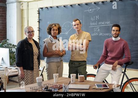 Row of young successful white collar workers in casualwear standing against blackboard and looking at camera in office Stock Photo
