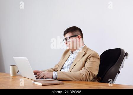 Contemporary businessman sitting in wheelchaair in front of laptop while analyzing online data in office Stock Photo