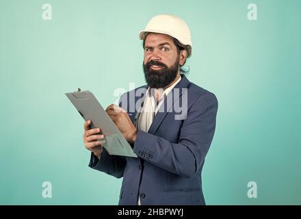 serious foreman in helmet and suit writing in paper folder, making notes Stock Photo