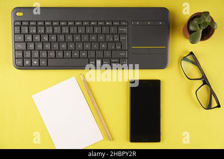 Flat lay shot of keyboard, smartphone, glasses, notepad and pencil on a yellow background Stock Photo