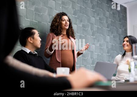 Pregnant businesswoman sharing business ideas with male and female colleagues during meeting Stock Photo