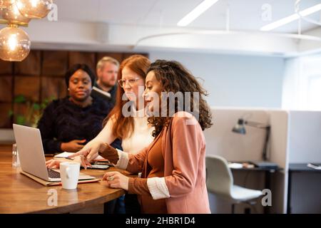 Pregnant businesswoman discussing with colleagues over laptop at office Stock Photo