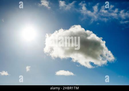 Die Sonne erstrahlt neben eíner imposanten Cumulus Wolke und wenigen Federwolken am blauen Himmel Stock Photo
