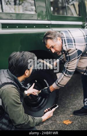 Father changing tire while talking with son on driveway Stock Photo