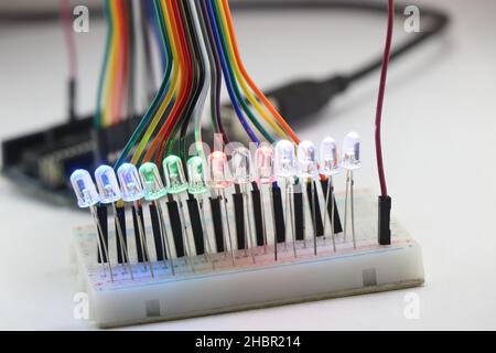 LED lights emitting multiple colors connected in a parallel circuit on a breadboard controlled by microcontroller connected with jumper wires Stock Photo