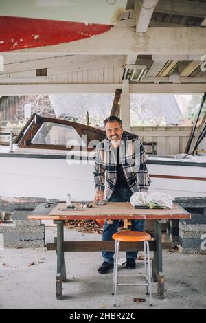 Portrait of mature man using smart phone at table in garage Stock Photo