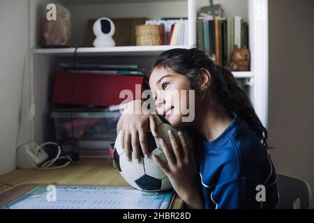 Contemplative girl looking away with soccer ball at table Stock Photo