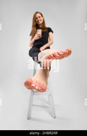 Young woman pulling her barefoot legs forward and making photo with her mobile phone (focus on foreground) Stock Photo