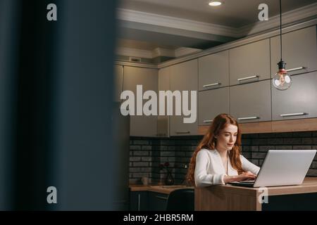 Woman typing on laptop at desk. Woman working in home office. Red haired woman. Self isolation. Stock Photo
