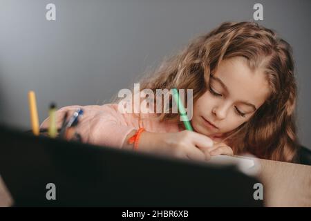 Close-up portrait of a caucasian schoolgirl doing her homework using gadgets for learning. Girl studying online. Distance education. Coronavirus. Stock Photo