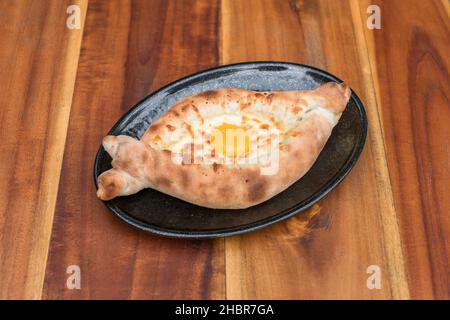 Traditional Georgian cuisine. Ajara khachapuri with egg on black plate on wooden background Top view, close up with copy space. High quality photo Stock Photo