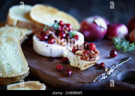 Toasted French bread with baked Camembert Brie cheese and cranberry, honey, balsamic vinegar and nut relish. Selective focus with blurred background. Stock Photo