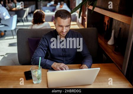 Young businessman is working on laptop in restaurant. Remote work. Stock Photo