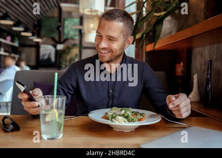 Smiling businessman is using his phone while having lunch in restaurant Stock Photo