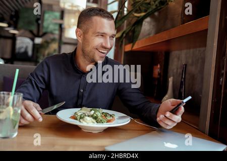 Smiling businessman is using his phone while having lunch in restaurant Stock Photo
