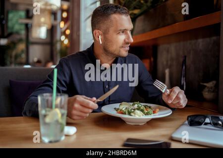 young businessman in EarPods is enjoying his lunch in restaurant. listening to music. Stock Photo