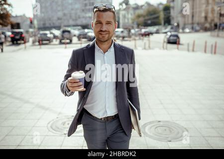 Young businessman holding his laptop while drinking coffee. Walking on the street. Stock Photo