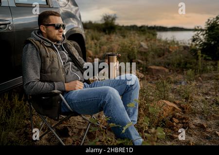 Young man is drinking tea while fishing. Outdoor picnic concept Stock Photo