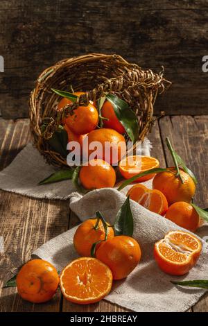 Tangerines falling out of the basket. Oranges, mandarins, clementines, citrus fruits) with green leaves. Wooden background, rustic style, close up Stock Photo