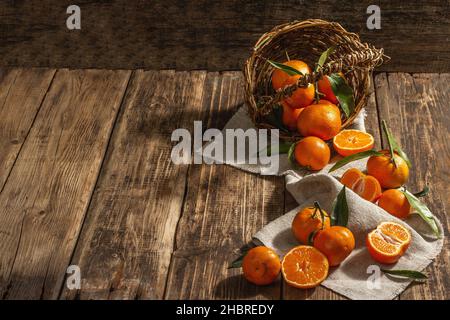 Tangerines falling out of the basket. Oranges, mandarins, clementines, citrus fruits) with green leaves. Wooden background, rustic style, copy space Stock Photo