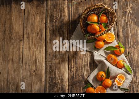 Tangerines falling out of the basket. Oranges, mandarins, clementines, citrus fruits) with green leaves. Wooden background, rustic style, top view Stock Photo