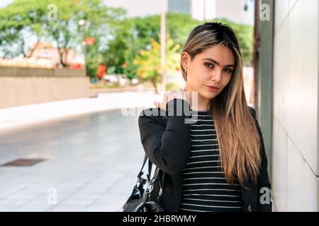 Beautiful enterprising woman standing with serious expression by the wall of an office building on a sunny day. Stock Photo
