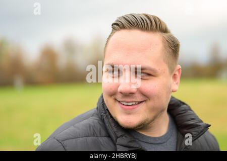 Young man looking aside with a quiet smile in a close up headshot outdoors in a park in autumn Stock Photo