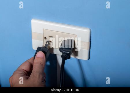 Man's hand plugging in a black wire. Latin, Colombian electrical outlet. Stock Photo
