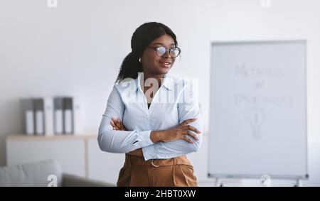 Psychological education. Successful business coach giving personal growth training, posing with crossed arms at office Stock Photo