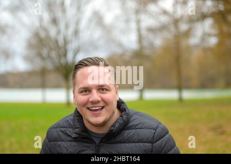 Laughing happy young man in an autumn park in a head and shoulders portrait as he looks at the camera Stock Photo