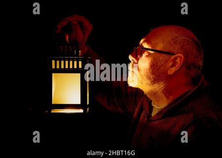 Grey haired man holding a lantern. low key lighting Stock Photo