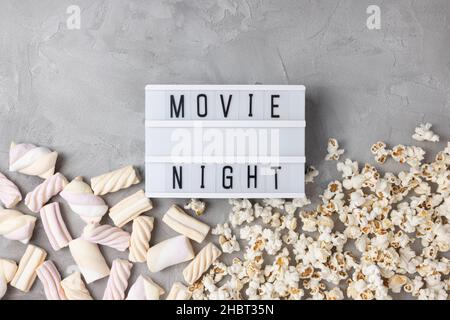 Text MOVIE NIGHT with popcorn and marshmallow on gray background. Cinema, movies, entertainment and snacks movie snacks at home concept. Top view, copy space Stock Photo