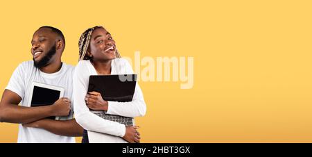 Gadget Addiction. Cheerful Black Man And Woman Embracing Digital Tablet And Laptop Stock Photo