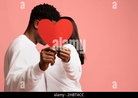 Unrecognizable black couple hiding behind red heart Stock Photo