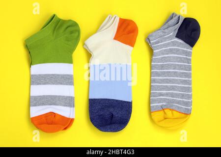 Short colored socks on a yellow background top view. Bright cotton socks for sports. Three pairs of striped colored short socks. Stock Photo