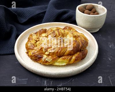 Cinnamon curls on a ceramic plate. Homemade puff pastry buns on a black background. A round bun sprinkled with almond flakes. Stock Photo