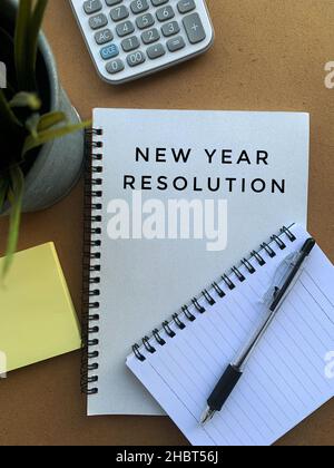 New year resolution text on note pad with pen, calculator, plant, sticky note and brown table background Stock Photo