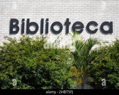 'Biblioteca' (Library) Written in Black Letters of a White Brick Wall above many Trees Stock Photo