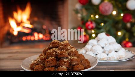 Christmas Greek melomakarona and kourabiedes, burning fireplace and Xmas tree background. Traditional homemade desserts. Stock Photo