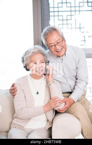 Happy old couple sitting on the sofa to talk on the phone Stock Photo