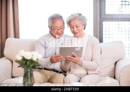 Happy old couple sitting on the sofa and using a tablet computer Stock Photo