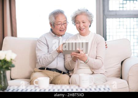 Happy old couple sitting on the sofa and using a tablet computer Stock Photo